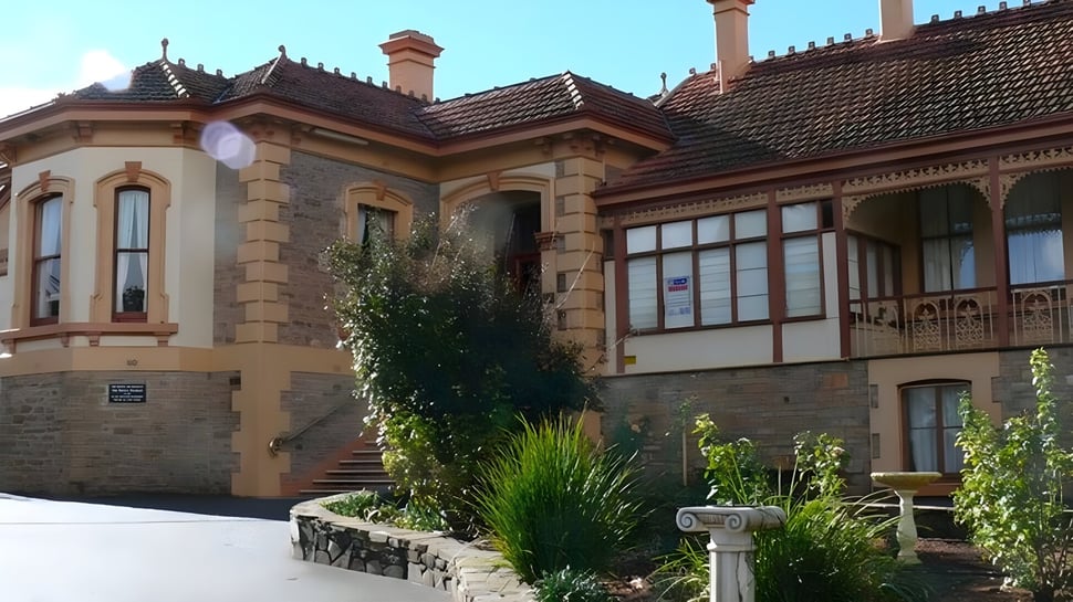 El histórico edificio principal de la Kapunda High School con un jardín en primer plano bajo un cielo azul.