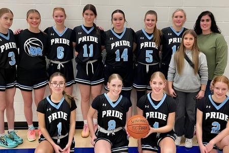 Un grupo de jóvenes jugadoras de baloncesto está reunido en el gimnasio de la Kate Andrews High School.