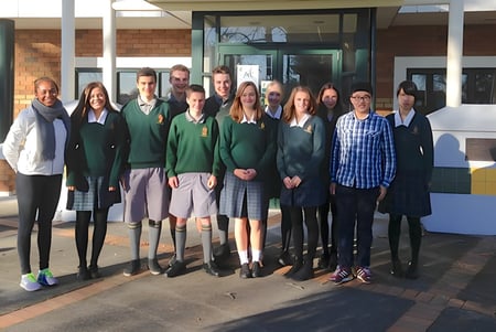 Un grupo de estudiantes está frente al edificio de ladrillo de Katikati College con una entrada de vidrio.
