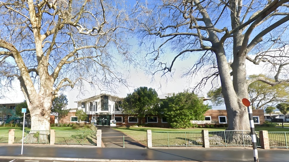El edificio histórico de Katikati College está rodeado de un terreno bordeado de árboles y una valla de hierro forjado.