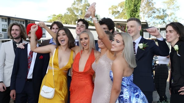 Un grupo de estudiantes de la Kedron State High School celebra juntos frente a los edificios escolares y árboles.