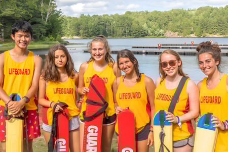 Un grupo de salvavidas está junto al lago en el campus de la Kedron State High School frente a árboles verdes.