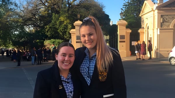 Dos estudiantes sonríen frente a un edificio histórico en el campus de la Keith Area School.