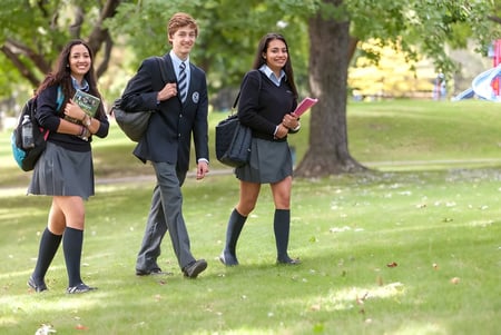 Tres estudiantes de Kells Academy caminan por un camino cubierto de hierba rodeado de árboles.