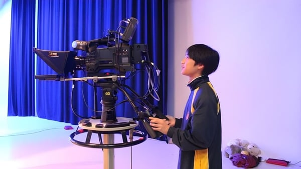 Un estudiante de la Kelmscott Senior High School está frente a una gran cámara de video con una cortina azul de fondo.
