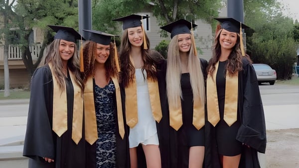 Cinco estudiantes de la Kelowna Secondary School están al aire libre en sus togas de graduación frente a un edificio escolar.