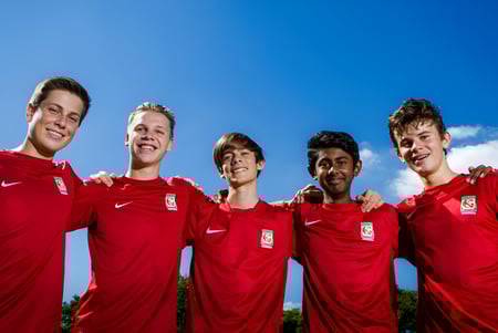 Un grupo de cinco estudiantes en camisetas de fútbol rojas está frente al cielo azul en el campus del Kelvin Grove State College.