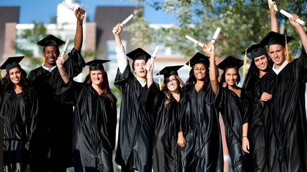 Un grupo de graduados celebra su ceremonia de graduación en el terreno de la Kelvin High School frente a árboles y edificios.