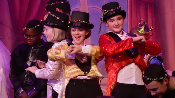 Un grupo de estudiantes del Kent College está en trajes coloridos en un escenario frente a una cortina roja.