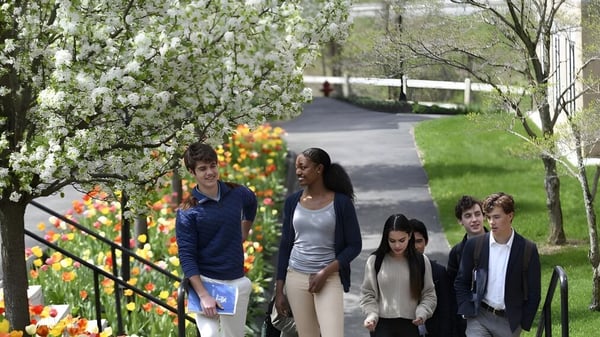 Un grupo de estudiantes de la Kent School pasea por un camino rodeado de árboles en flor y flores de colores.