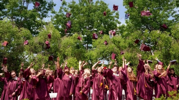 Un grupo de graduados de Kents Hill School en togas burdeos celebra su graduación bajo árboles verdes.