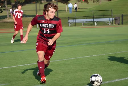 Un jugador de fútbol con camiseta roja dribla el balón en el campo de la Kents Hill School.