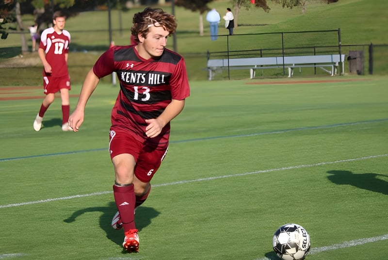 Un jugador de fútbol con camiseta roja dribla el balón en el campo de la Kents Hill School.