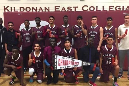 El equipo de baloncesto de Kildonan East Collegiate posa junto con un trofeo frente a un cartel de la escuela.