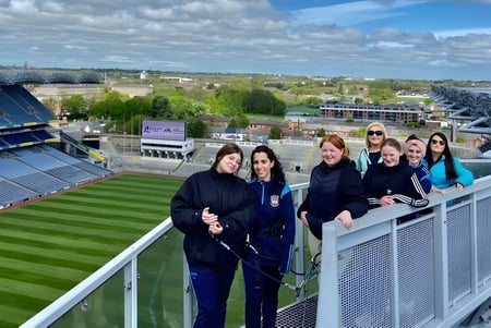 Estudiantes de la Kilkenny City Vocational School están en un balcón con vista a un gran estadio deportivo y la ciudad de fondo.