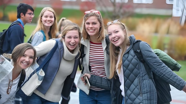 Un grupo de estudiantes sonrientes de la Kimball Union Academy está afuera en invierno frente a edificios de ladrillo.