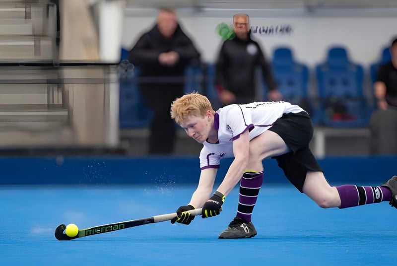 Una persona juega al hockey sobre césped en el campo de césped artificial azul de la Kimbolton School frente a un grupo de espectadores.