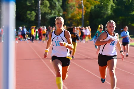 Dos atletas corren en la pista en el terreno de Kincoppal-Rose Bay frente a espectadores y árboles.