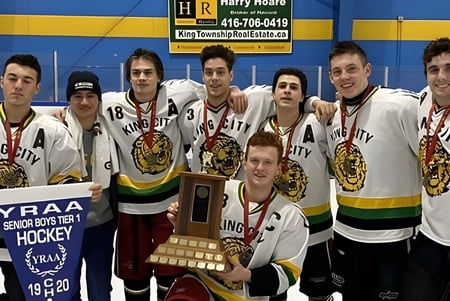 Estudiantes de la King City Secondary School posan con trofeos frente a un fondo azul y amarillo después de un partido de hockey.