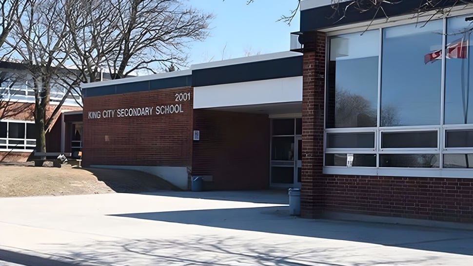 El edificio de ladrillo de la King City Secondary School está rodeado de árboles y un camino pavimentado conduce a la entrada.
