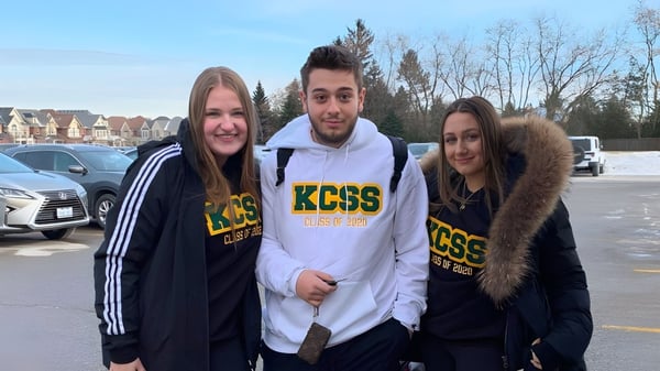 Tres estudiantes están juntos en el área exterior de la King City Secondary School con casas residenciales al fondo.