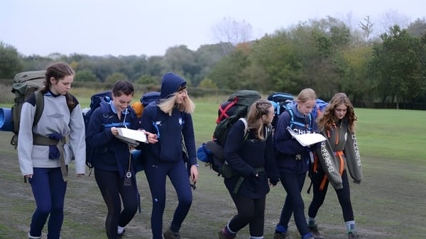 Un grupo de estudiantes de la King Edward's Witley School se reúne en un campo de hierba entre árboles.