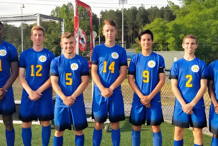 Un grupo de jóvenes futbolistas en camisetas azules está en el campo de deportes de la King George Secondary School.