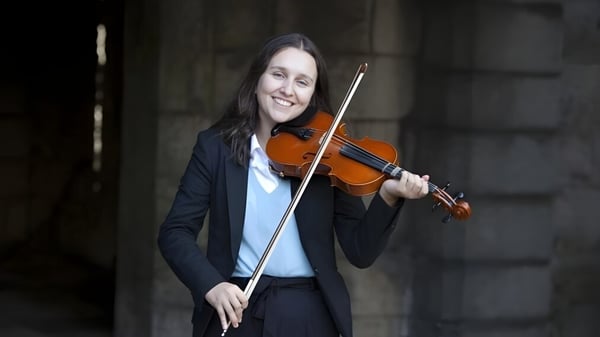 Una persona toca el violín en el campus del King William's College frente a un fondo oscuro.