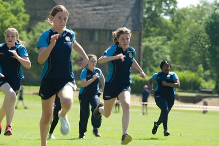 Un grupo de jóvenes atletas corre juntos en un campo deportivo en el campus de la Kingham Hill School.