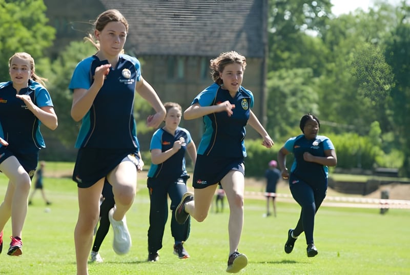 Un grupo de jóvenes atletas corre juntos en un campo deportivo en el campus de la Kingham Hill School.