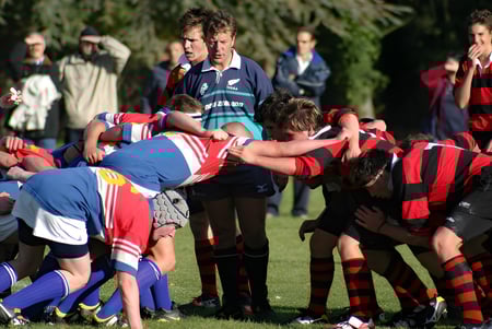 Estudiantes del King's College juegan un scrum de rugby en el campo con espectadores al fondo.