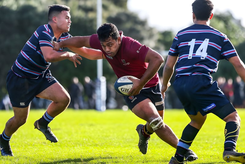 Tres jugadores de rugby realizan un intenso momento de tackle en un campo del King's College.