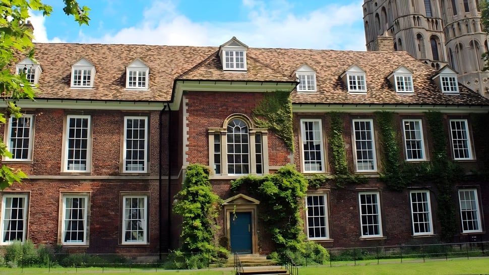 El histórico edificio de ladrillo con techo de tejas en el campus de King's Ely está rodeado de vegetación verde.
