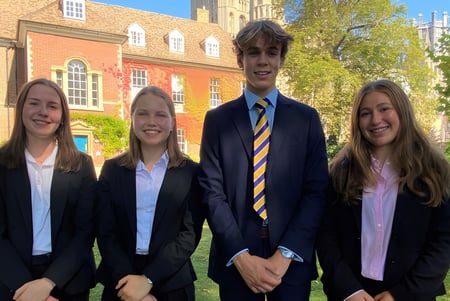 Cuatro alumnas y alumnos están de pie frente a un histórico edificio de ladrillo en el campus de King's Ely.