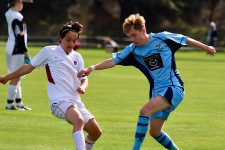 Dos estudiantes de la King's High School juegan al fútbol en un campo con otros jugadores al fondo.