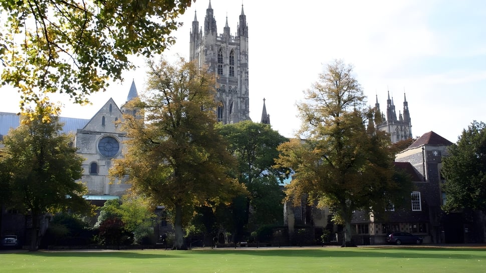 La histórica catedral con árboles de colores otoñales en el terreno de la King's School bajo un cielo despejado.