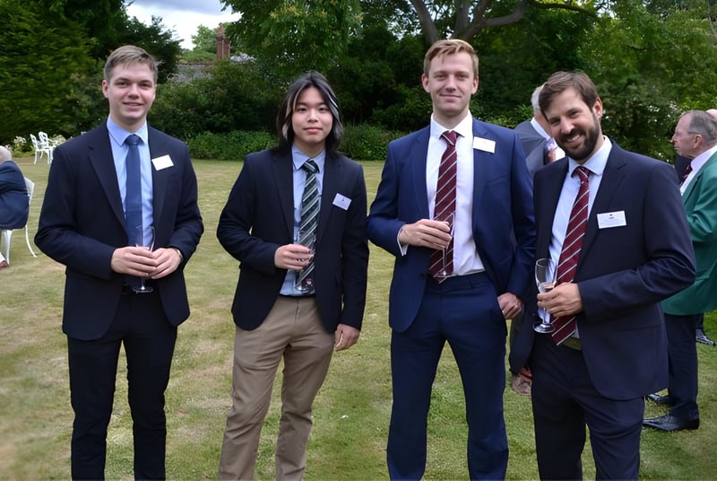 Cuatro hombres en ropa formal están juntos en un campo en el terreno de la King's School.