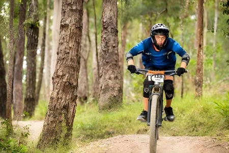 Un estudiante de la Kingscliff High School monta una bicicleta de montaña en un sendero del bosque.