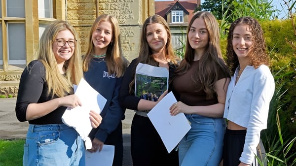 Cinco alumnas de la Kingsley School están juntas frente a un antiguo edificio de piedra con hierba al fondo.