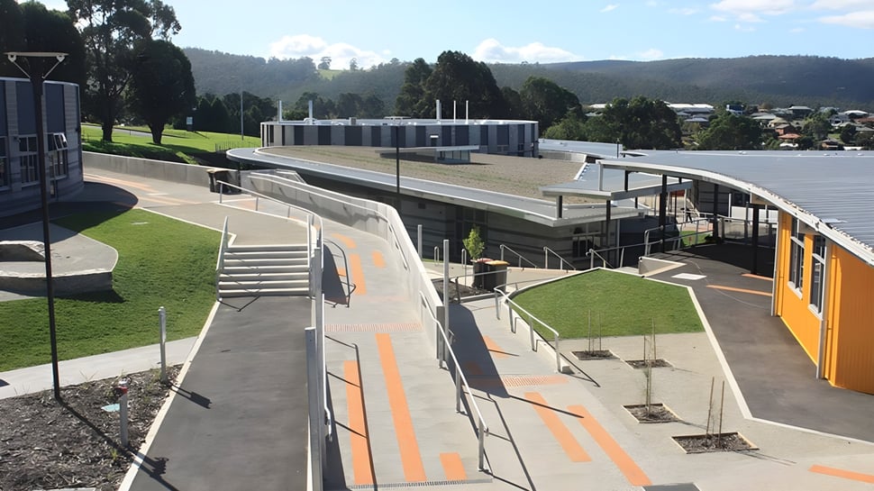 El moderno edificio de varios pisos de la Kingston High School, con escaleras y rampas, está rodeado de áreas de césped y árboles.