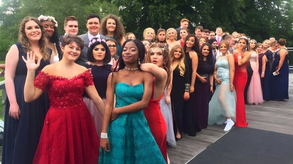 Estudiantes de la Kingston High School se reúnen vestidas de gala en una plataforma de madera con un entorno verde.