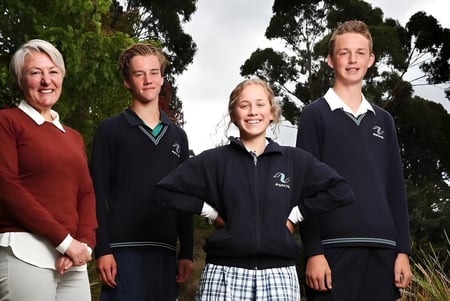Cuatro personas están de pie afuera, frente a árboles, en el terreno de la Kingston High School.