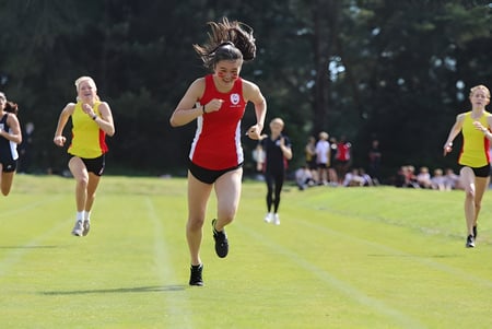 Un grupo de corredoras de la Kingswood School participa en una carrera en un campo cubierto de hierba.