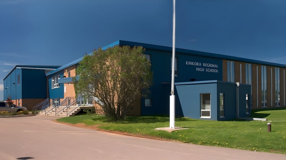 El moderno edificio escolar de la Kinkora Regional High School con un prado verde y un camino pavimentado en primer plano bajo un cielo azul.