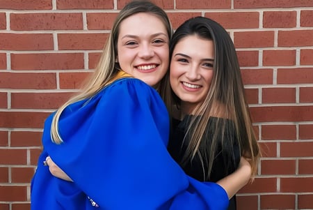 Dos alumnas de la Kinkora Regional High School se abrazan frente a una pared de ladrillo.