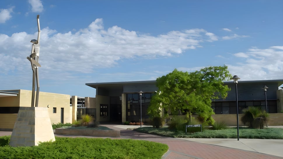 El moderno edificio de Kinross College con un patio diseñado y rodeado de árboles bajo un cielo azul.