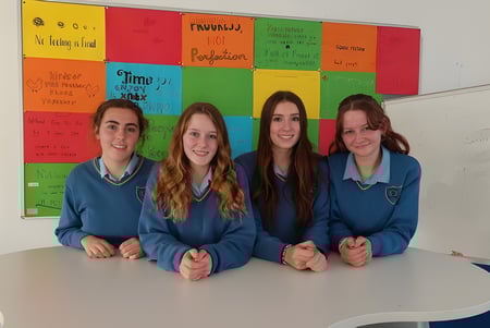 Cuatro alumnas de la Kinsale Community School están sentadas en un aula colorida alrededor de una mesa.