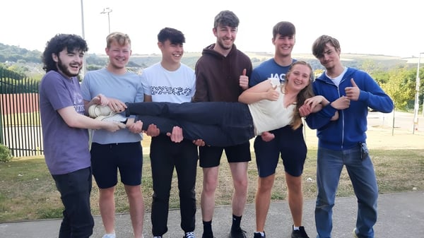 Un grupo de alumnos está al aire libre en un prado detrás de una cerca en el terreno de la Kinsale Community School.