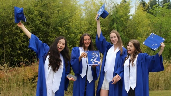 Cuatro estudiantes de la Kitsilano Secondary School celebran su graduación en togas azules en el bosque.