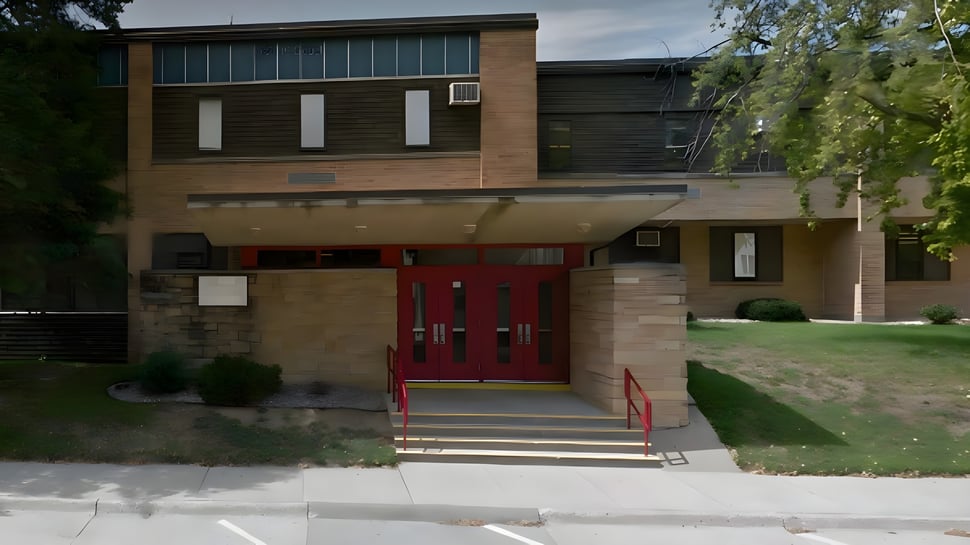 El moderno edificio de varios pisos de la Kuemper Catholic High School con entrada roja y ventanas de vidrio frente a un prado verde.